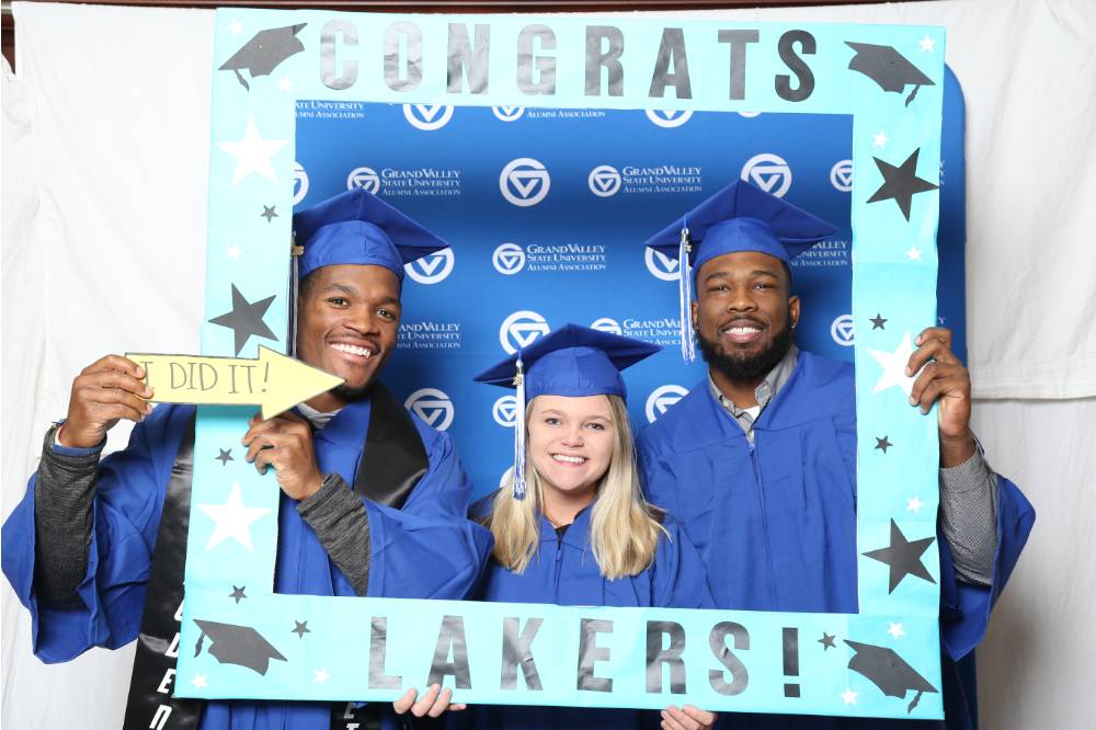 Three upcoming alumni pose with a frame at Gradfest